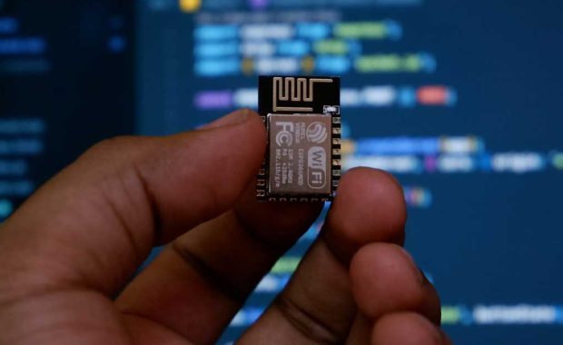 Mano mostrando un chip delante de una pantalla de ordenador